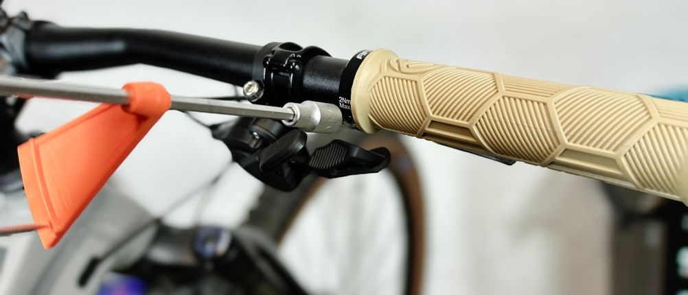 Ein Fifty-Fifty-MTB-Griff wird mit einem Drehmomentschlüssel an einem schwarzen Lenker befestigt. Im Hintergrund steht ein Mountainbike.