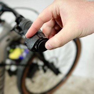 Eine Hand setzt die Endkappe der Reetee-Fahrradgriffe in das Lenkerende ein. Das Fahrrad steht im Hintergrund unscharf im Bild.