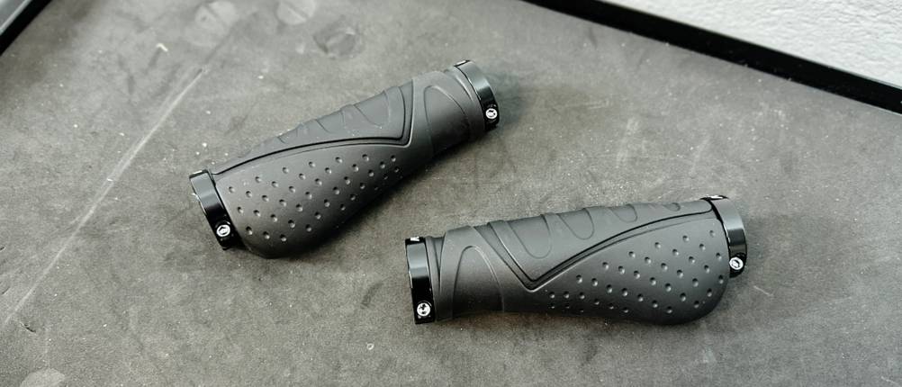 Zwei Reetee-Fahrradgriffe mit ergonomischer Form und verschraubbaren Endkappen liegen auf einer Werkbank.