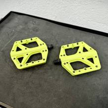 Zwei Crankbrothers Stamp 1 Pedale in leuchtendem Gelb liegen nebeneinander auf einer Werkbank. Die Pins sind bereits vormontiert.