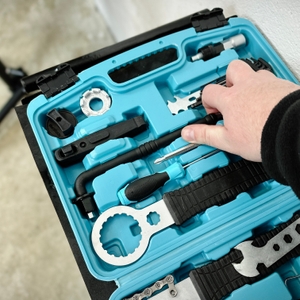 Eine Hand greift nach einem Schraubendreher aus einem blauen Werkzeugkoffer. Das Set enthält Spezialwerkzeug für Fahrradreparaturen.