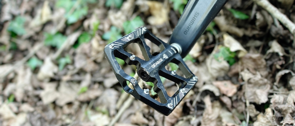 Ein Gewage USGE323 Pedal montiert an einem Mountainbike im Wald. Die schwarze Optik hebt sich vom hellen Laub ab.