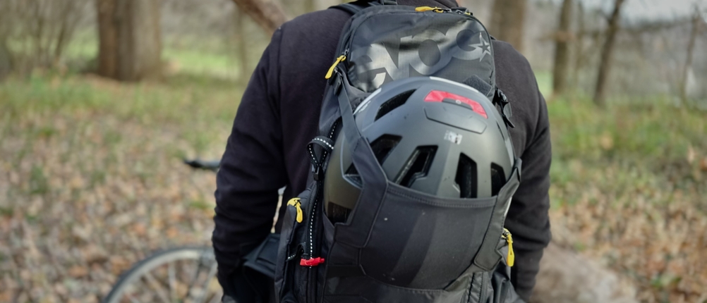 Ein Mann trägt den MTB-Rucksack von Evoc mit Helmhalterung auf dem Rücken.