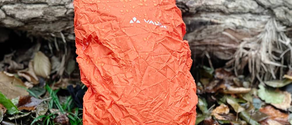 Der MTB-Rucksack von Vaude ist mit Schutzhülle versehen, lehnt an einem Baumstamm im Wald und wird beregnet.