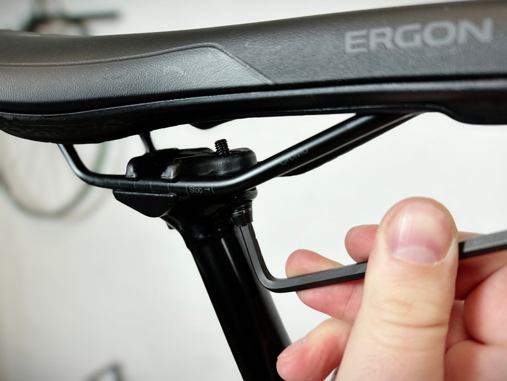 Nahaufnahme eines Ergon SMC Core MTB-Sattels während der Montage. Eine Hand hält einen Inbusschlüssel, um die Sattelklemme an der Sattelstütze zu befestigen.