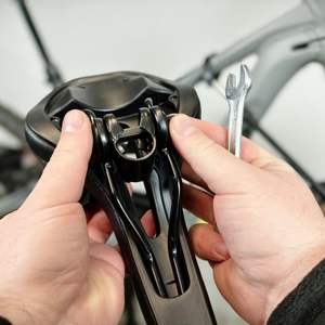 Der Youngdo MTB-Sattel wird von seiner originalen Sattelaufnahme gelöst. Eine Hand hält den Sattel, während die Schrauben entfernt werden.