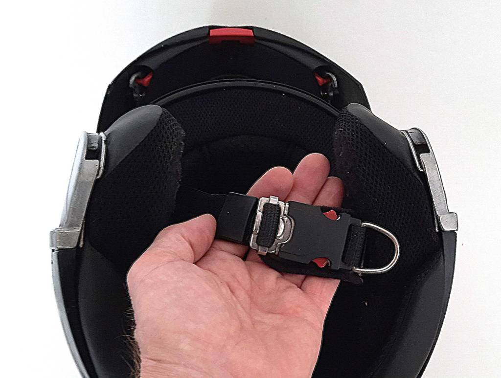 Eine Hand hält den Clickverschluss eines getesteten Motorradhelms.