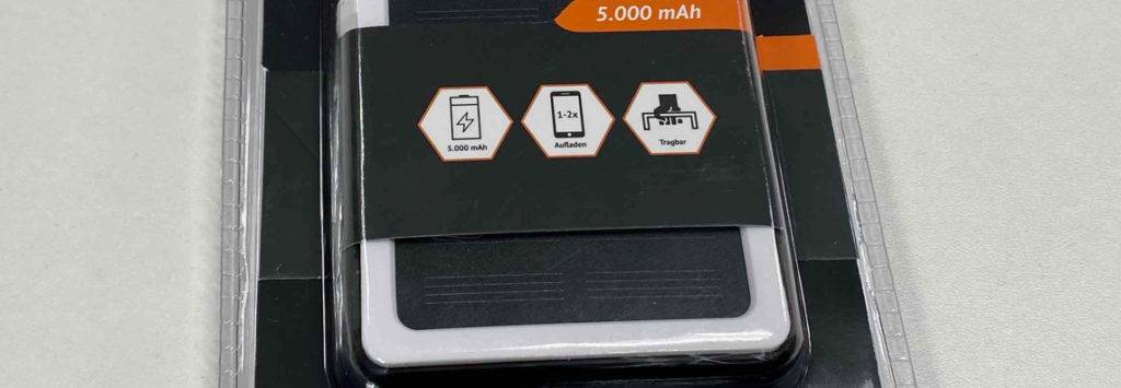 Eine weiße Müller Solar-Powerbank im Test in weißem Design liegt in seiner durchsichtigen Verpackung auf einer weißen Fläche.