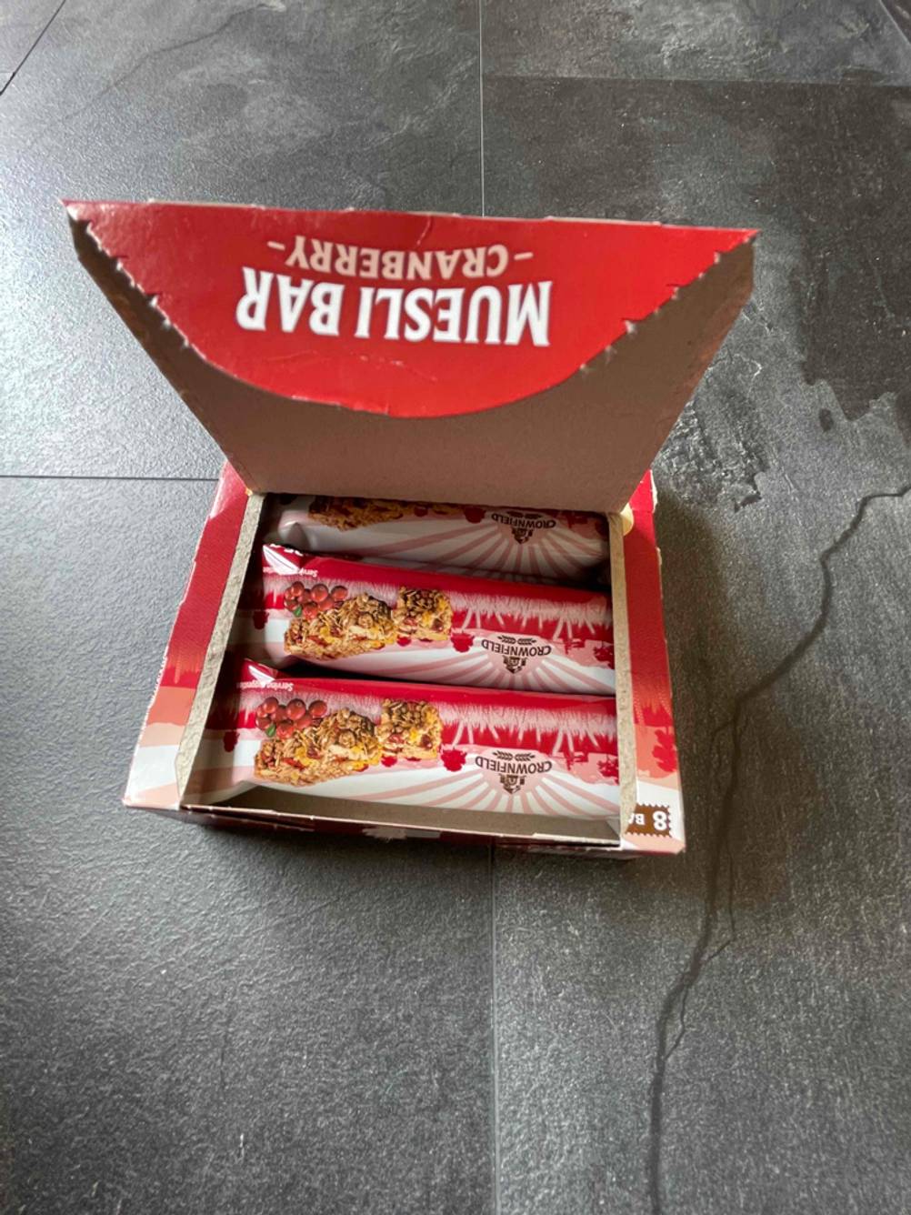 Im Test: Eine offene Verpackung mit mehreren verpackten Müsliriegeln darin auf einer dunklen Fläche.