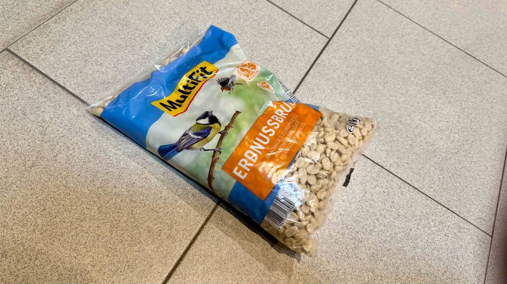 Eine Packung Vogelfutter-Erdnüsse liegt zum testen auf einem hellen Fliesenboden.