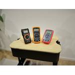 Drei getestete Multimeter stehen auf einem Rollwagen nebeneinander.