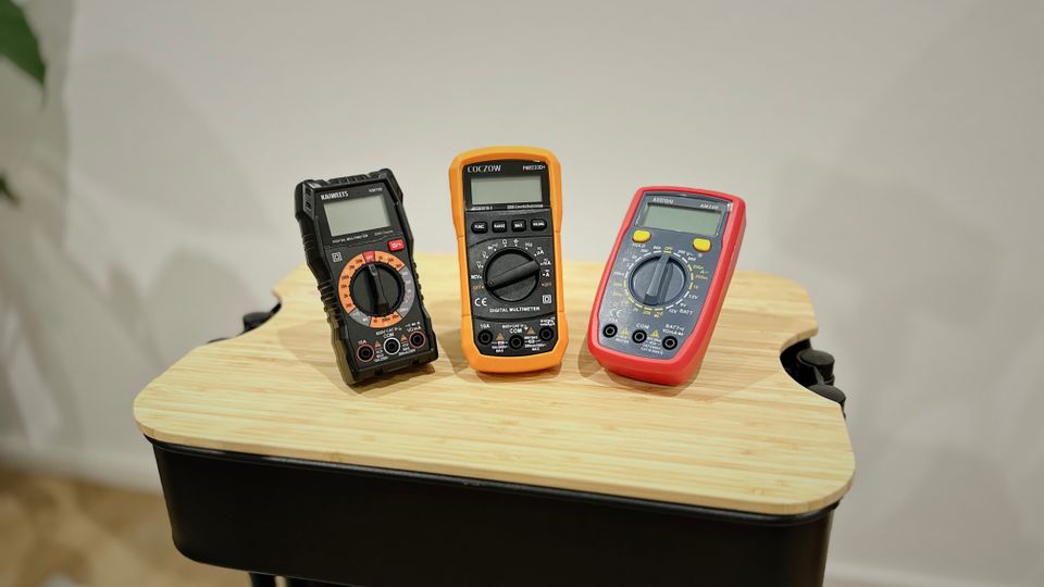 Drei getestete Multimeter stehen auf einem Rollwagen nebeneinander.