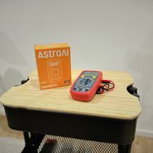 Das Multimeter von AstroAI liegt neben seiner Verpackung inkl. Kabel auf einem Rollcontainer.