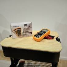 Das Multimeter von Coczow liegt neben seiner Verpackung inkl. Kabel auf einem Rollcontainer.