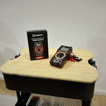 Das Multimeter von Kaiweets liegt neben seiner Verpackung inkl. Kabel auf einem Rollcontainer.