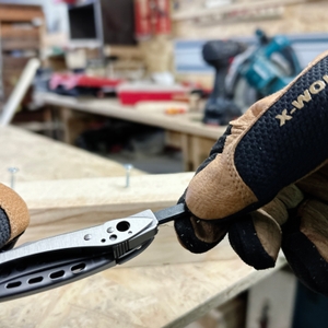 Eine Hand hält das Leatherman Skeletool, während die andere ein Doppelbit hält. Im Hintergrund ist eine Metallkonstruktion zu sehen.