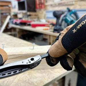 Eine Hand hält das Leatherman Skeletool, während die andere ein Doppelbit hält. Im Hintergrund ist eine Metallkonstruktion zu sehen.