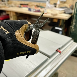 Das Leatherman Skeletool Multitool wird von einer Hand mit einem schwarzen Arbeitshandschuh der Marke Kinetix gehalten. Die Edelstahlzange ist geöffnet und zeigt die präzisen Zangenbacken.