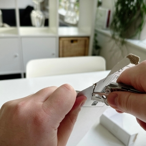 Zwei Hände schneiden mit dem Leatherman Skeletool einen Karton auf. Der Hintergrund zeigt eine helle, modern eingerichtete Wohnung.