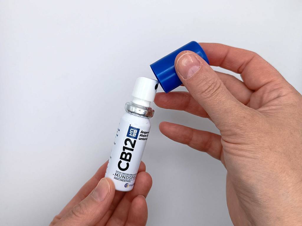 Hand nimmt die Kappe eines Mundsprays zum testen ab.