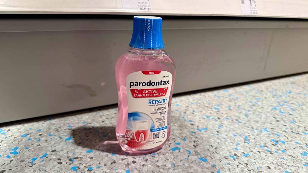Eine Flasche der Mundspülung gegen Zahnfleischentzündung im Test vor einem Regal auf dem Boden stehend.
