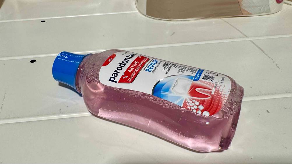 Seitenansicht einer Flasche der getesteten Mundspülung gegen Zahnfleischentzündung auf einer hellen Fläche liegend.