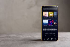 Musik-Streaming-Test: Auf einem grauen Untergrund steht ein Smartphone, auf dem ein Musik-Streaming-Dienst geöffnet ist.