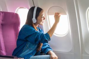 Musik-Streaming-Test: Eine junge Frau trägt Kopfhörer, während Sie in einem Flugzeug lächelnd aus dem Fenster schaut.