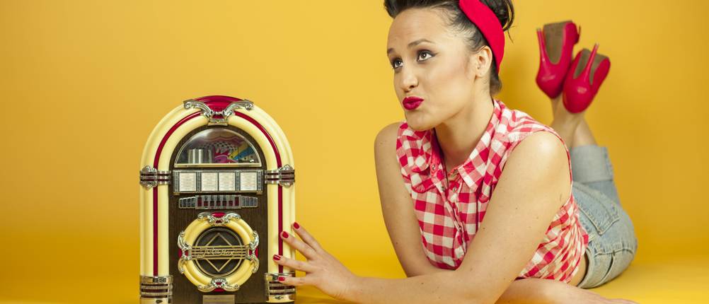 Eine Frau im Pin Up-Stil liegt neben einer Jukebox und entscheidet sich für einen eigenen Musikbox-Test.