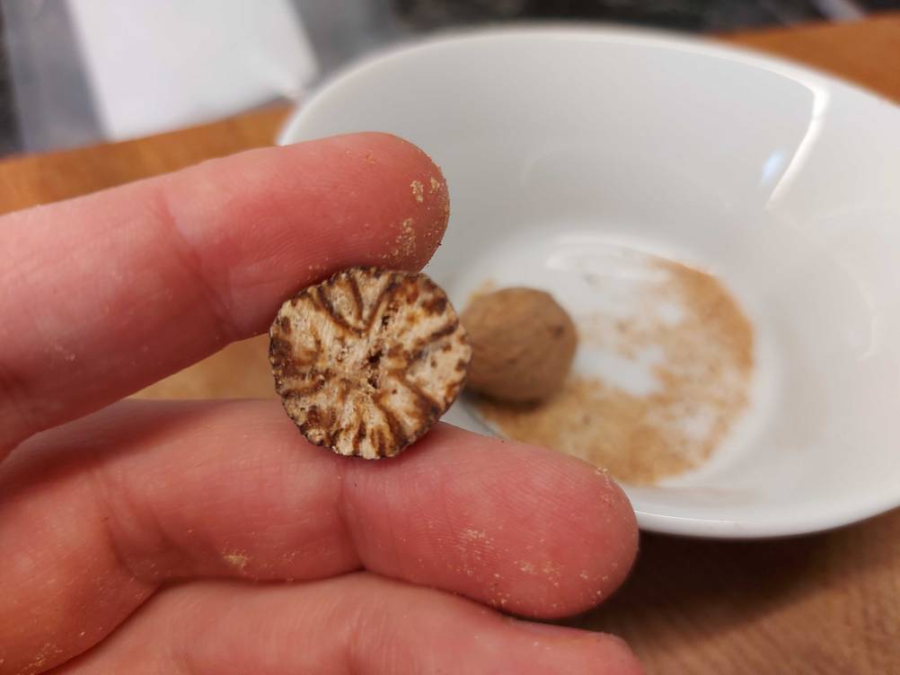 Eine Hand hält eine halbe Muskatnuss im Test vor eine weiße Schüssel.