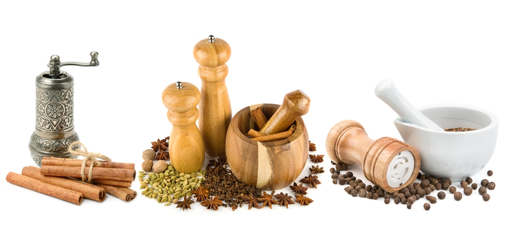 Reihe an verschiedenen Gewürzen und Mühlen vor weißem Hintergrund.