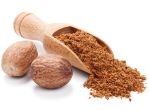 Zwei Muskatnüsse liegen neben einer Holzschippe mit gemahlener Muskatnuss.