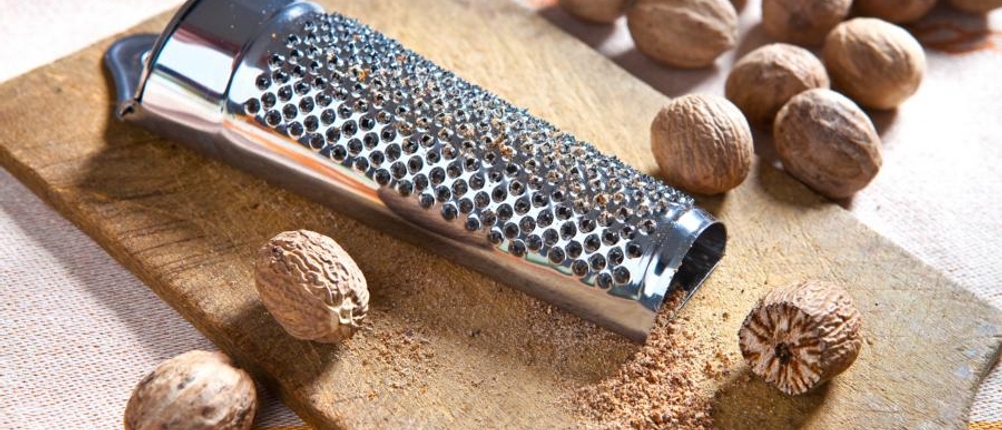 Eine Muskatreibe liegt zusammen mit Muskatnüssen auf einem Brett