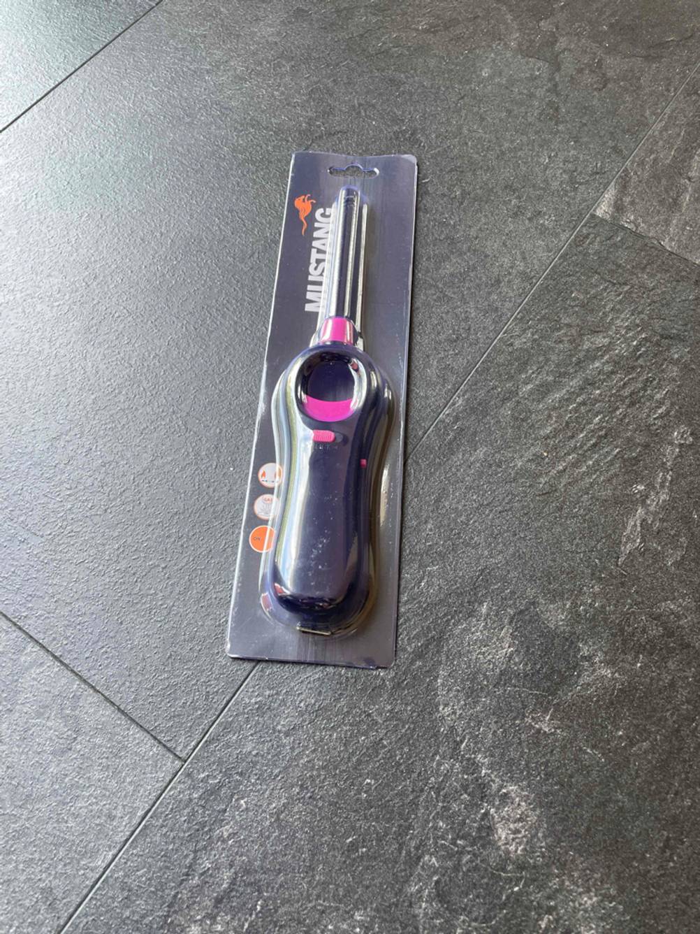 Ein Stabfeuerzeug liegt verpackt zum testen auf einem schwarzen Boden.
