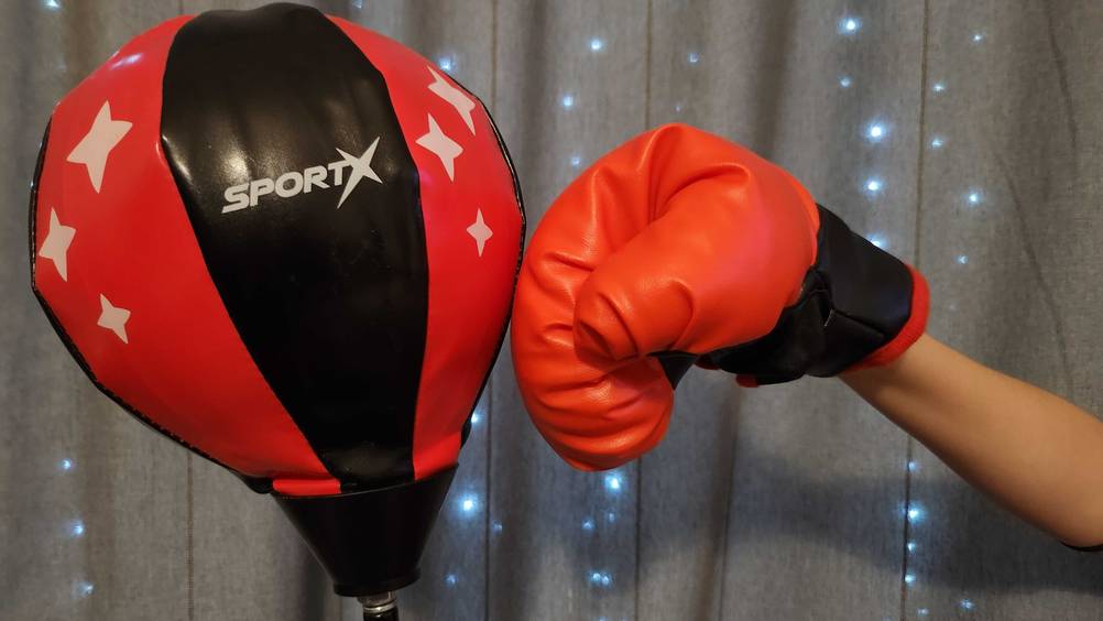 Eine Kinderfaust im roten Boxhandschuh schlägt auf einen getesteten Kinder-Boxsack.