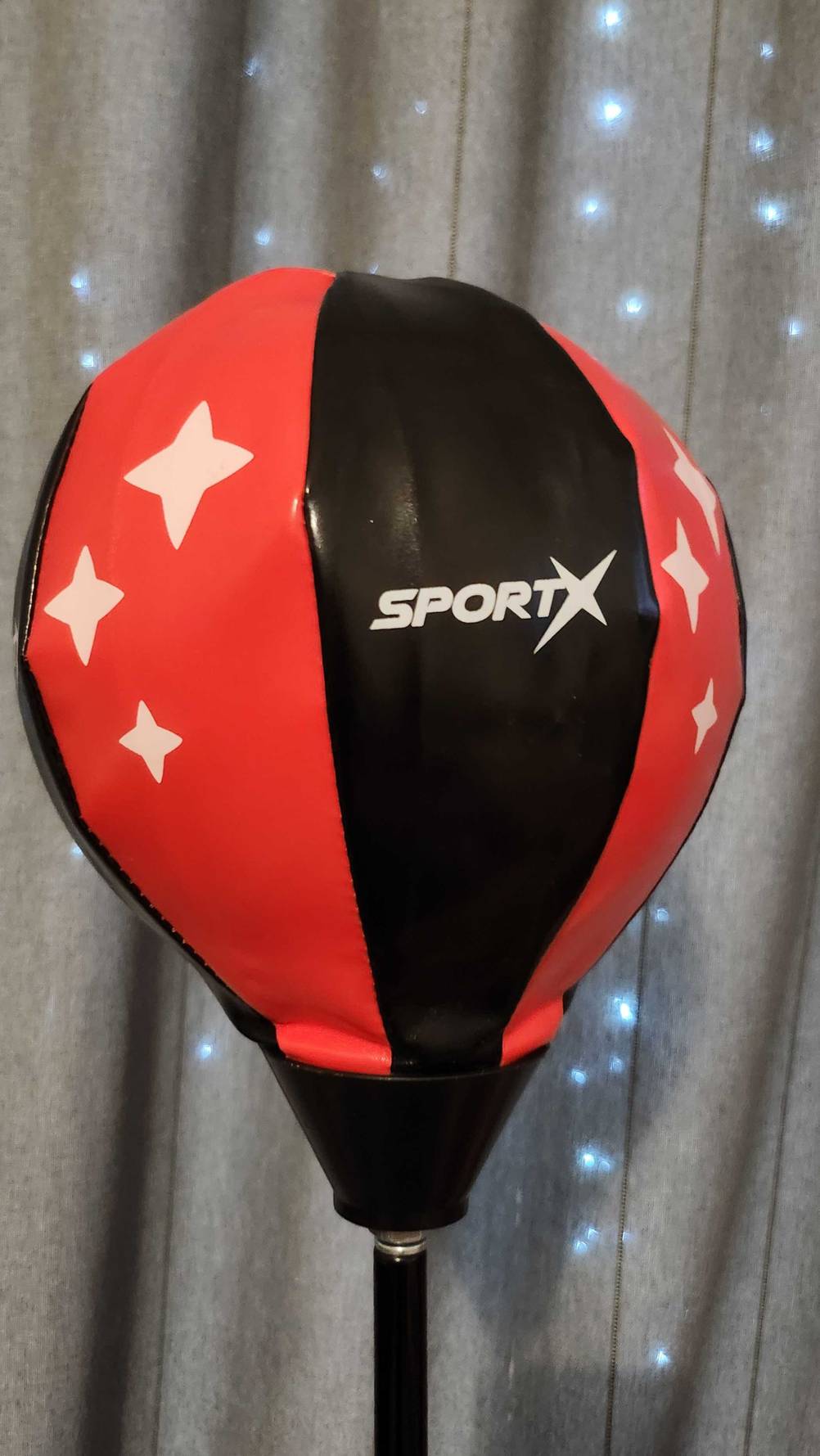 Ein getesteter Kinder-Boxsack in Rot-schwarz befindet sich vor einem beleuchteten Vorhang.
