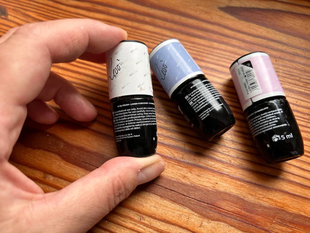 Hand hält eine von drei auf einem Tisch liegenden Nagellacken