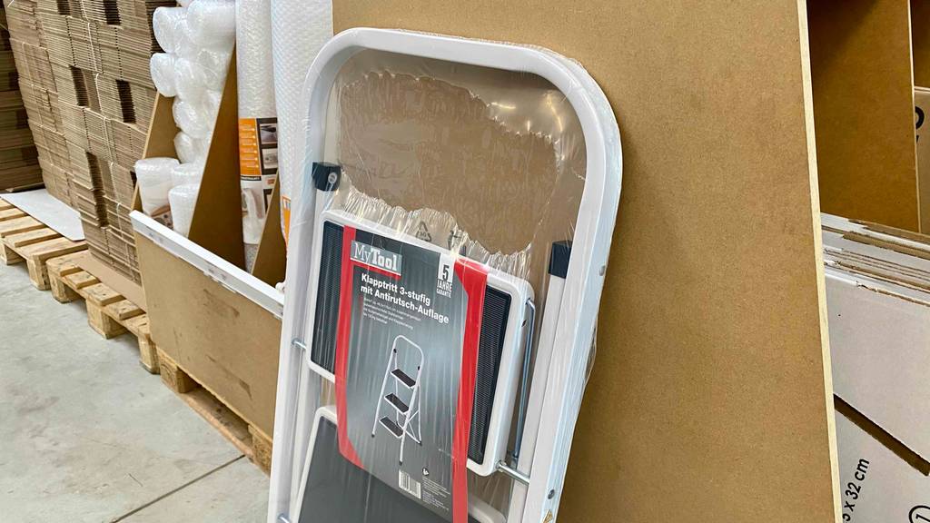 Getestet: Eine Trittleiter mit 3 Stufen, eingeschweißt in einer Kunststoffverpackung, befindet sich im Verkaufsbereich eines Baumarkts.