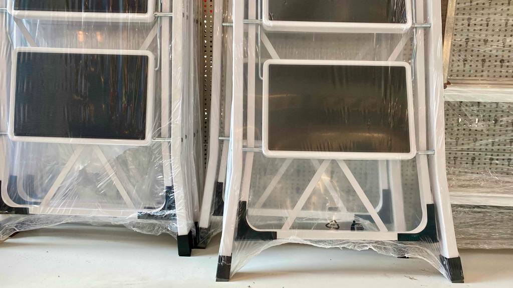 Mehrere weiße 3-Stufen-Trittleitern im Test mit schwarzen, gummierten Trittflächen steht in transparentem Kunststoff eingeschweißt in einem Verkaufsbereich.