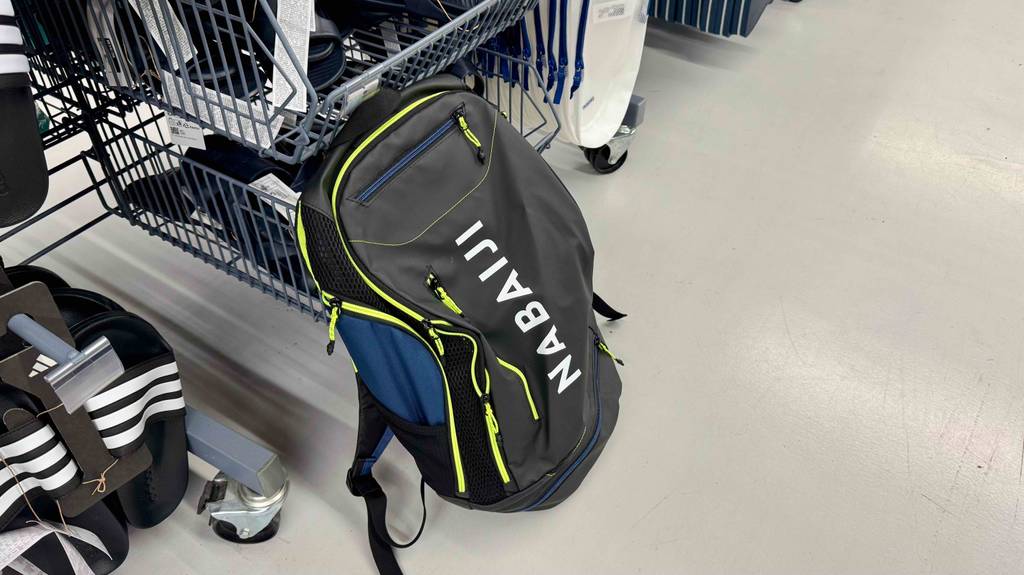 Ein dunkler, getesteter Schwimmrucksack der Marke Nabaiji hängt an einem Verkaufsregal, in dem sich Badesachen befinden.