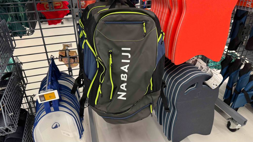 Ein dunkler, mit mehreren Reißverschlussfächern ausgestatteter Schwimmrucksack im Test hängt an einem Verkaufsregal zwischen Schwimmbrettern.