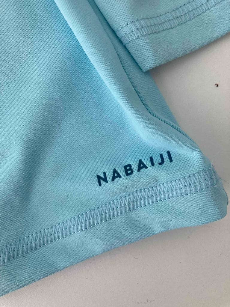 Nahaufnahme des Markenzeichens NABAIJI am Arm des hellblauen, getesteten UV-Shirts für Kinder.