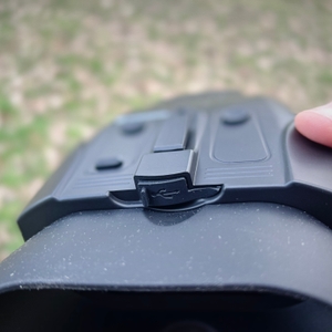 Der Anschlussbereich des Bresser Digital NV Binokulars zeigt eine geschützte Ladebuchse. Eine Hand hält das Gerät, der Hintergrund ist unscharf.