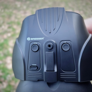 Nahaufnahme der Bedienelemente des Bresser-Digital-NV-Binokulars mit den Tasten für Zoom, Infrarot und Power. Eine Hand hält das Gerät.