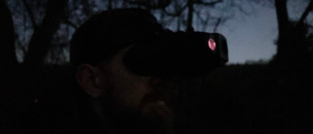 Ein Mann nutzt das Bresser-Digital-NV-Binokular 1x mit Kopfhalterung bei Dunkelheit. Die Infrarotstrahler des Geräts leuchten leicht rötlich.