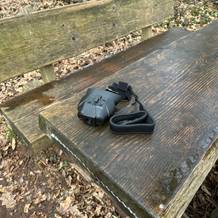 Das Bresser Digital NV Binokular 1x mit Kopfhalterung liegt mit Zubehör auf einer Holztischplatte. Im Lieferumfang sind eine Kopfhalterung und ein Trageband enthalten.