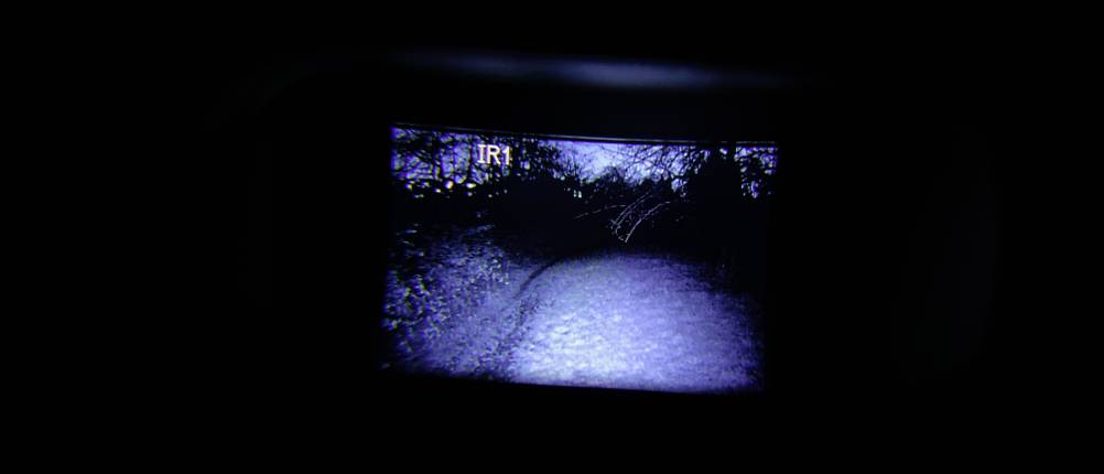 Das Display des Bresser-Digital-NV-Binokulars 1x mit Kopfhalterung zeigt eine nächtliche Landschaft in Schwarz-Weiß. Im Bild ist der IR-Modus 1 aktiviert.