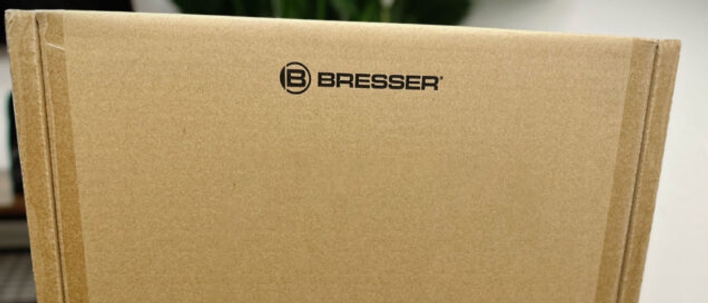 Die Verpackung des Bresser-Digital-NV-Binokular 1x mit Kopfhalterung steht auf einem Tisch. Der Karton zeigt das Bresser-Logo und ein Versandetikett.