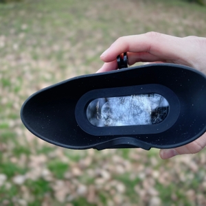 Die Innenseite des Nightfox-Swift-Nachtsichtgeräts zeigt das Display mit einer Reflexion des Himmels. Eine Hand hält das Gerät, der Hintergrund ist unscharf.