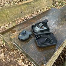 Das Nightfox Swift Nachtsichtgerät liegt mit Zubehör auf einer Holzbank. Im Lieferumfang sind eine Kopfhalterung und eine Tragetasche enthalten.